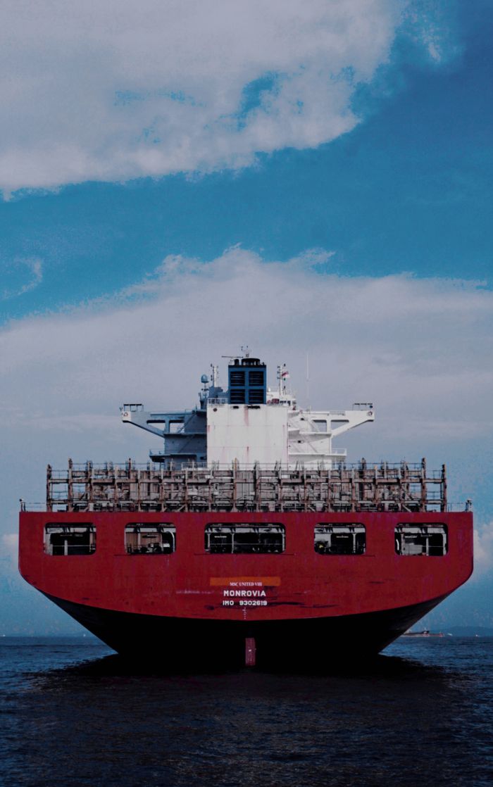Large red cargo ship transporting goods across the ocean under a bright blue sky.